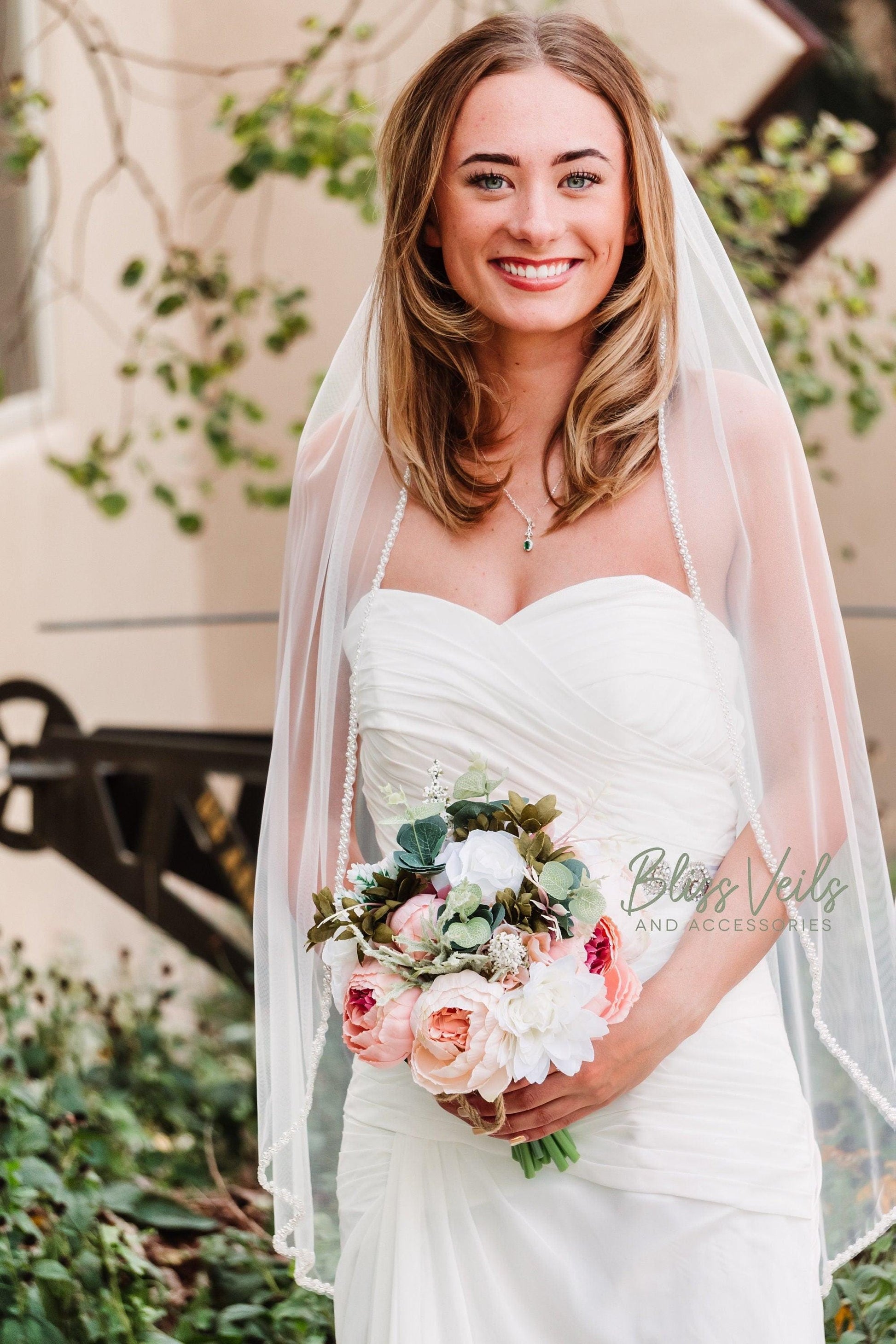 Bride wearing a pearl beaded wedding veil in soft tulle, fingertip length with one-tier design in soft white or light ivory